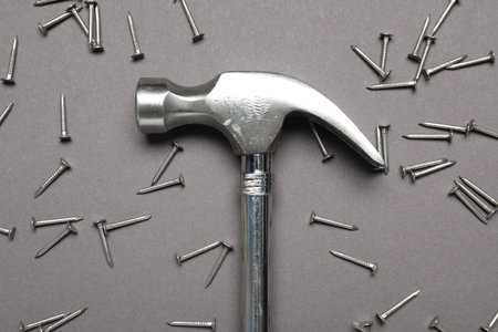 Hammer and metal nails on gray background, top view