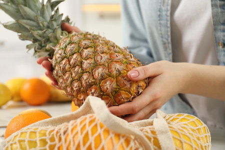 Woman taking pineapple out from string bag at table, closeupの写真素材