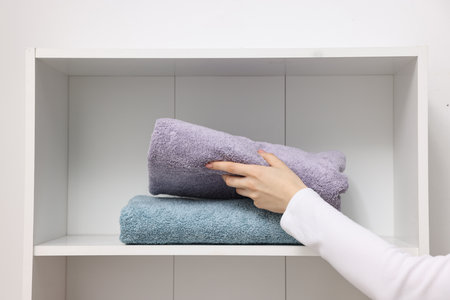 Woman stacking clean towels on shelf indoors, closeupの写真素材