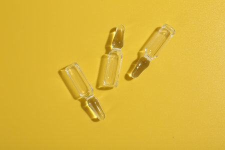 Glass ampoules with liquid on yellow background, flat layの写真素材