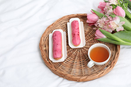 Tasty breakfast served in bed. Delicious eclairs, tea and flowers on wicker tray, above view with...