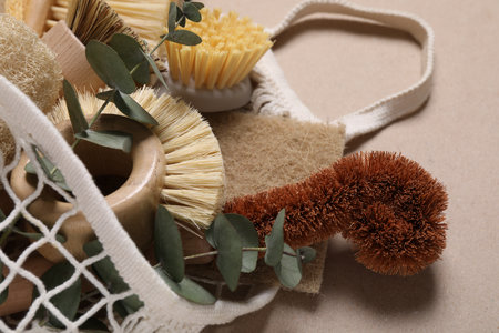 Cleaning brushes, sponges, eucalyptus leaves and string bag on pale brown background, closeupの写真素材