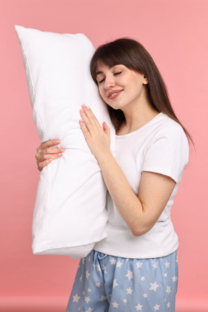 Happy woman in pyjama holding pillow on pink background