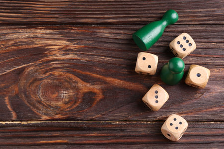 Many dices and green game pieces on wooden table, flat lay. Space for text