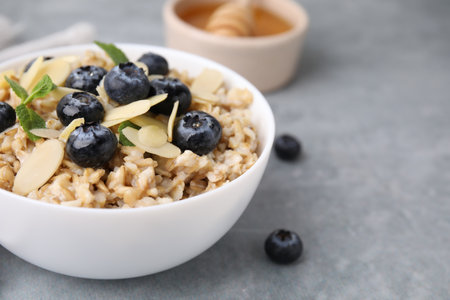 Tasty oatmeal with blueberries, mint and almond petals in bowl on gray table, closeup. Space for textの写真素材
