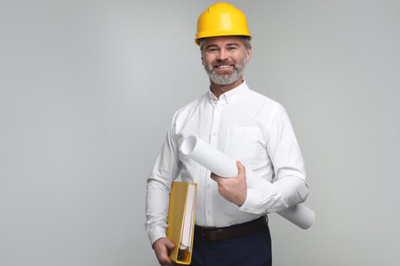 Architect in hard hat holding folder and draft on grey background