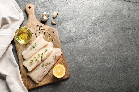 Raw cod fish, microgreens, oil, spices and lemon on gray textured table, top view. Space for text