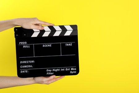Woman holding movie clapper on yellow background, closeup. Space for textの写真素材