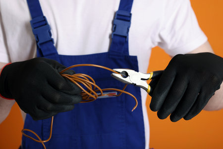 Young man holding pliers and wires on orange background, closeupの写真素材