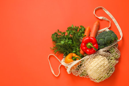 String bag with fresh vegetables and herbs on coral background, top view. Space for text