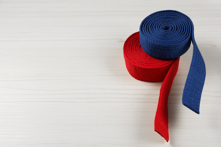 Colorful karate belts on wooden background, space for text