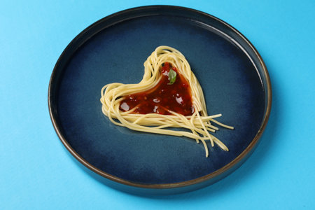 Heart made with spaghetti and sauce on light blue background