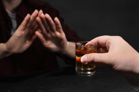 Alcohol addiction. Woman refusing glass of whiskey at dark table, selective focusの写真素材