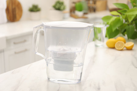 Water filter jug, glass and lemons on white marble table in kitchenの写真素材
