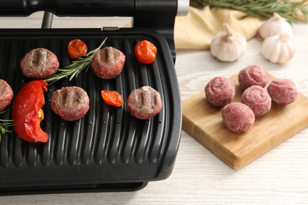 Electric grill with vegetables, meat balls and rosemary on wooden tableの写真素材