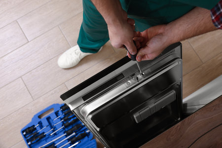 Serviceman repairing dishwasher's door with screwdriver indoors, closeupの写真素材