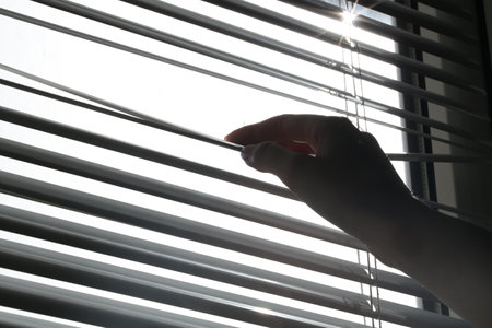 Woman separating slats of white blinds indoors, closeupの写真素材