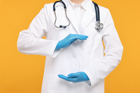 Doctor with stethoscope holding something on orange background, closeupの写真素材