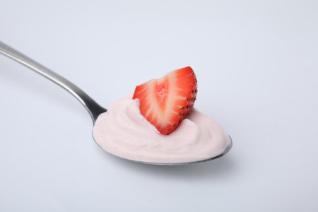 Delicious natural yogurt with fresh strawberry in spoon on light backgroundの写真素材