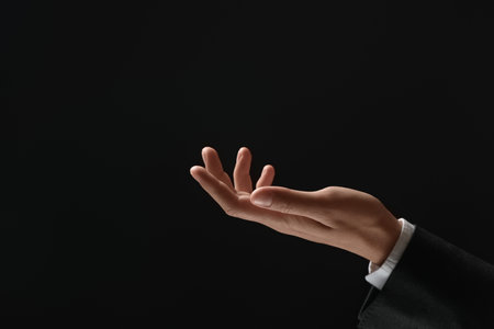 Man holding something in hand on black background, closeup. Space for textの写真素材