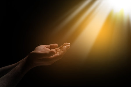 Christian man stretching hands towards holy light in darkness, closeup. Prayer and beliefの写真素材
