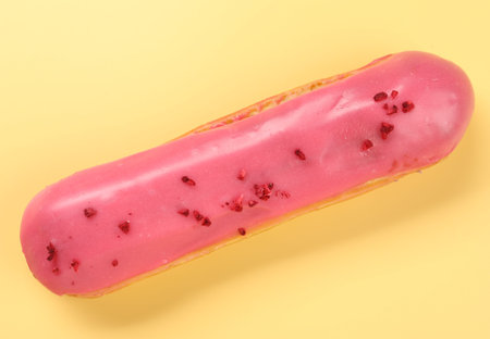 Delicious eclair covered with glaze on yellow background, top view