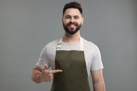 Smiling man pointing at kitchen apron on grey background. Mockup for designの写真素材