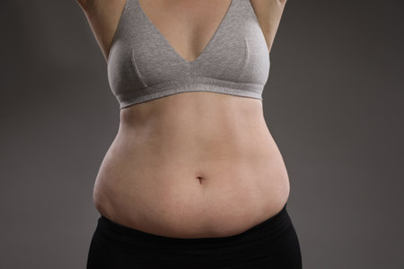 Woman with excessive belly fat on gray background, closeup. Overweight problemの写真素材