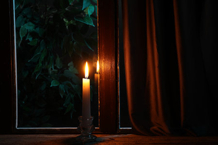 Burning candle on wooden table near window at nightの写真素材