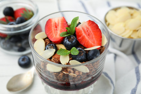 Tasty granola with berries, jam and almond flakes in glass on white table, closeupの写真素材