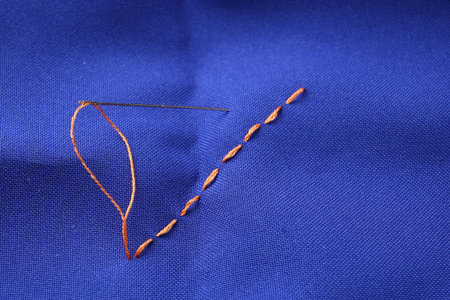 Sewing needle with thread and stitches on blue cloth, above view