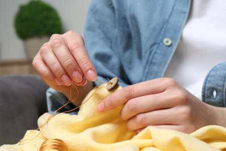 Woman sewing button with needle and thread onto shirt at home, closeupの写真素材