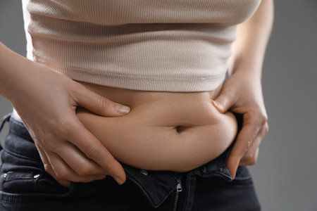 Woman touching belly fat on gray background, closeup. Overweight problemの写真素材