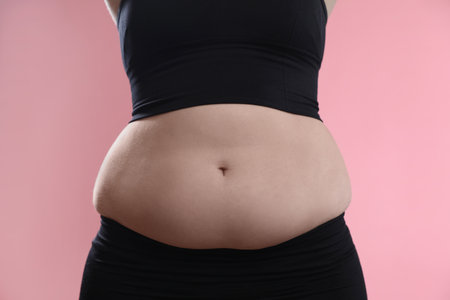 Woman with excessive belly fat on pink background, closeup. Overweight problemの写真素材