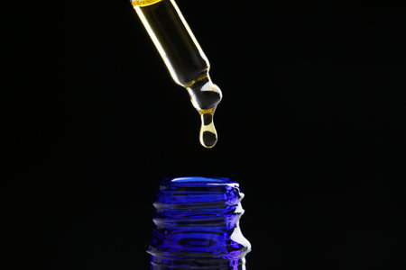 Dripping tincture from pipette into bottle on black background, closeup