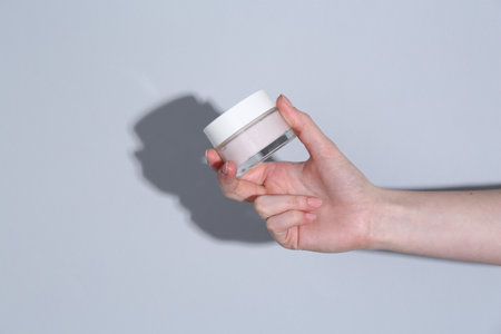 Woman holding jar of cream on gray background, closeup. Space for text