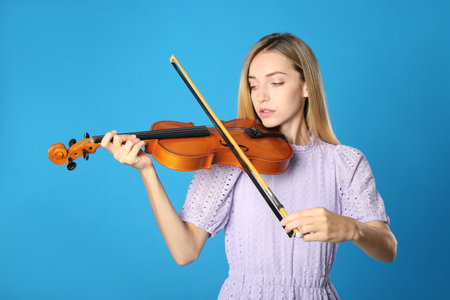 Beautiful woman playing violin on blue backgroundの写真素材