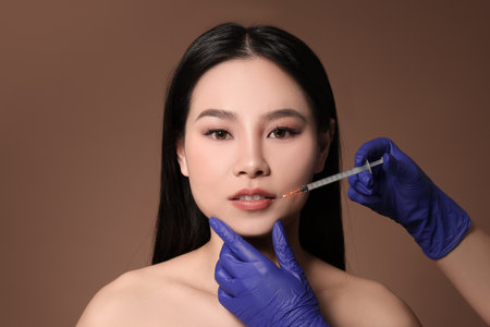 Woman getting lip injection on brown backgroundの写真素材