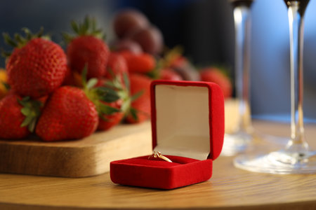 Engagement ring and fresh strawberries on wooden table, closeup. Romantic dinner