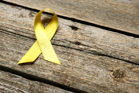 Yellow awareness ribbon on wooden table, above view. Space for textの写真素材