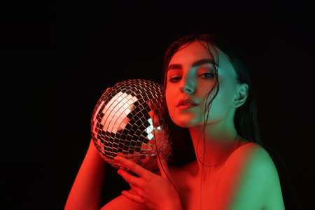 Beautiful woman with disco ball posing in neon lights against black background