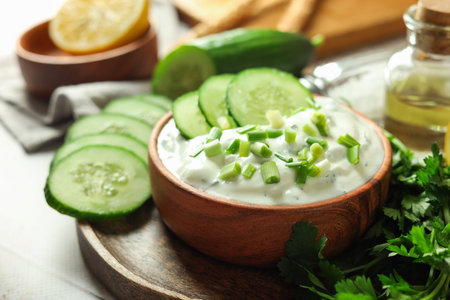 Delicious yogurt with green onion, cucumbers and parsley on light table, closeupの写真素材