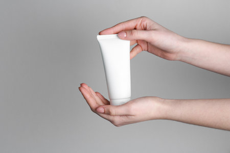 Woman holding tube of cream on gray background, closeup. Space for textの写真素材