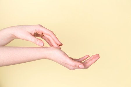 Woman applying cream on her hand against yellow background, closeupの写真素材