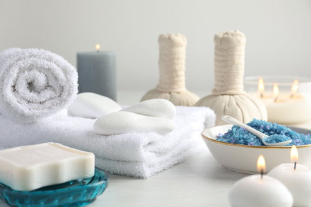 Spa composition. Towels, herbal bags, soap, sea salt and burning candles on light tableの写真素材