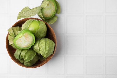 Fresh green tomatillos with husk in bowl on white tiled table, flat lay. Space for textの写真素材