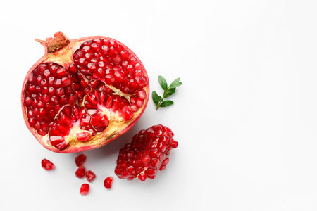 Cut fresh pomegranate and green leaves on white background, flat lay. Space for textの写真素材