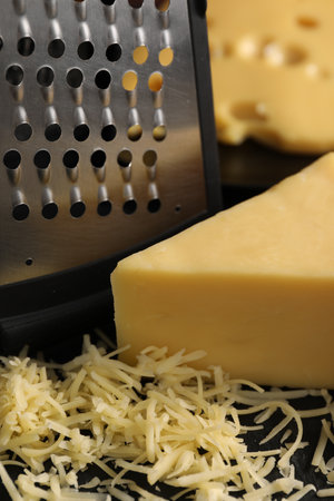 Grated, cut cheese and grater on black table, closeupの写真素材