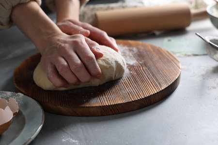 Woman kneading dough at gray table, closeup