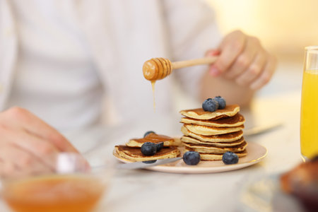 Man pouring honey onto pancakes with blueberries at table, closeupの写真素材